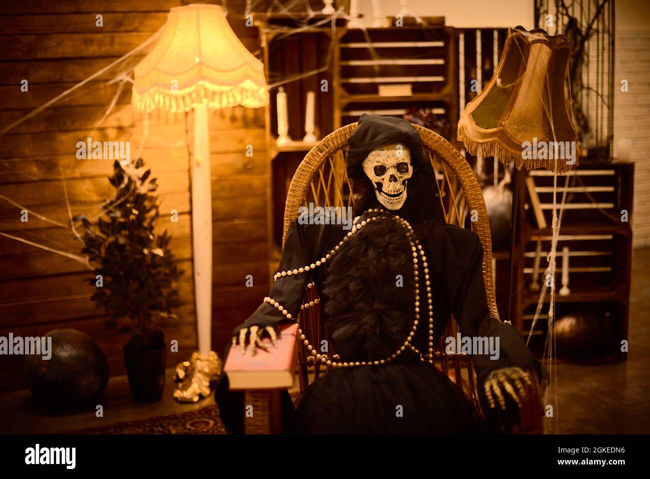 esqueleto de miedo de mujer vestida de cabo negro se sienta en la silla por la noche en halloween Foto de stock