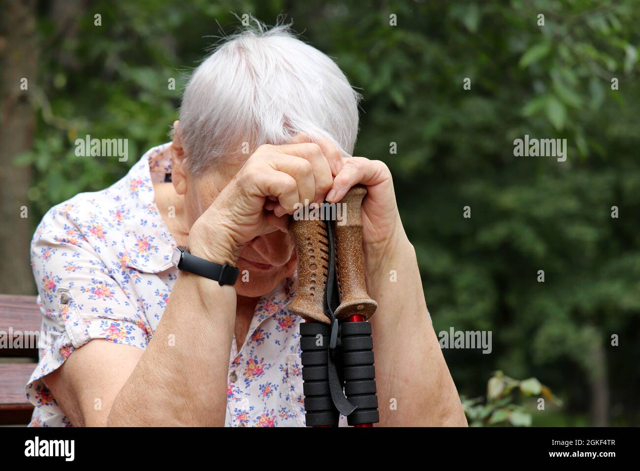 Mujer mayor sentada con la cabeza abajo en palos de paseo sobre un banco. Enfermedad y cansancio, estilo de vida saludable en la vejez, vida en la jubilación Foto de stock