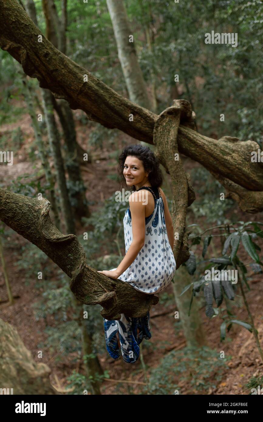 La chica se sienta en una enorme rama de liana en la selva. Foto de stock