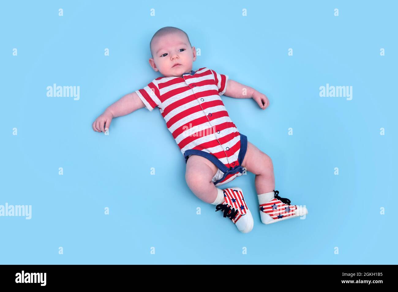 Un bebé recién nacido vestido con los colores de la americana de los Estados Unidos, fondo azul del estudio. Un niño en la ropa los EE.UU. Rojo blanco