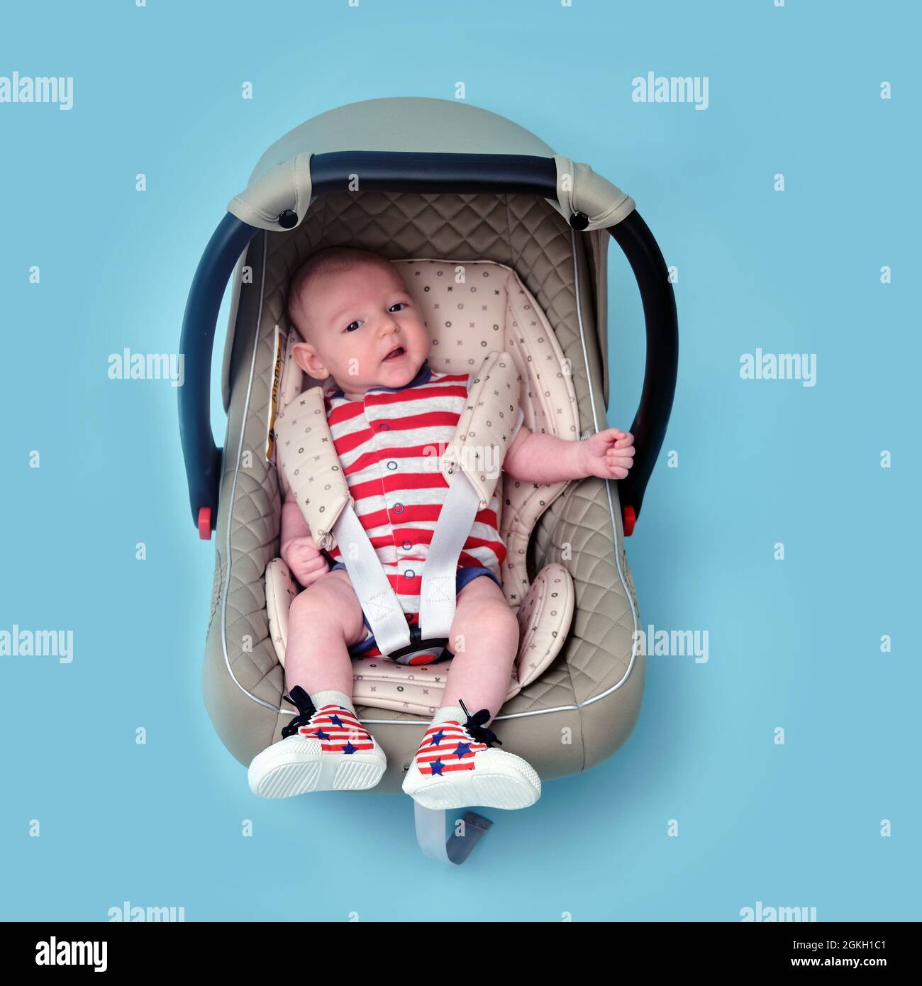 Bebé en el asiento de seguridad para niños sobre fondo azul del estudio. Niño en de la bandera roja y blanca de los Estados Fotografía de stock - Alamy