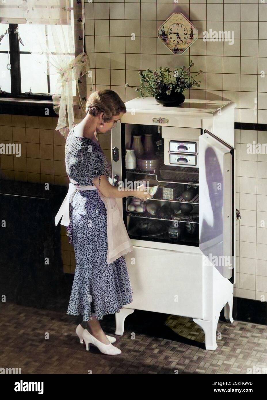 1920S 1930S RUBIA MUJER EN DELANTAL SEDA VESTIDO DE FIESTA TACONES ALTOS  TOMANDO PLATO DE COCINA ELÉCTRICA NEVERA - Q74782C CPC001 HARS MUJERES  GROWNUP HOGAR VIDA COPIA ESPACIO DE LONGITUD COMPLETA SEÑORAS
