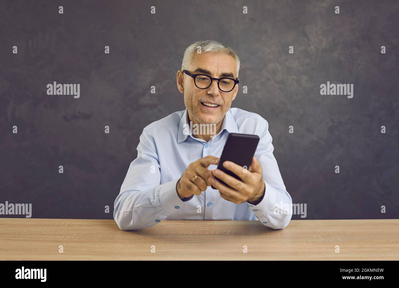 El hombre mayor sonriente escribe un mensaje o navega por las noticias en Internet utilizando un teléfono móvil moderno. Foto de stock