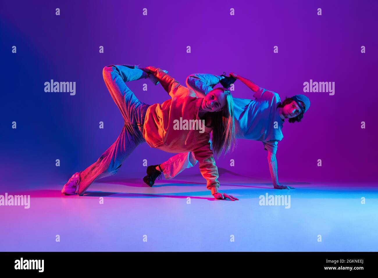 Hombre joven y mujer bailando hip-hop en ropa juvenil deportiva informal  sobre fondo rosa púrpura degradado en la sala de baile con luz de neón  Fotografía de stock - Alamy