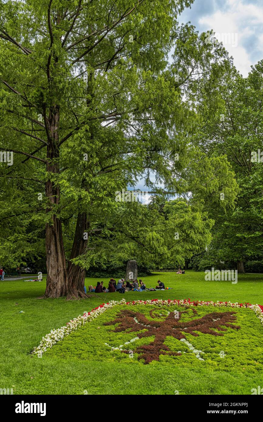 Grupo de jóvenes sentados en la hierba a la sombra de un árbol en los jardines paisajistas del palacio imperial. Innsbruck, Tirol, Austria, Europa Foto de stock