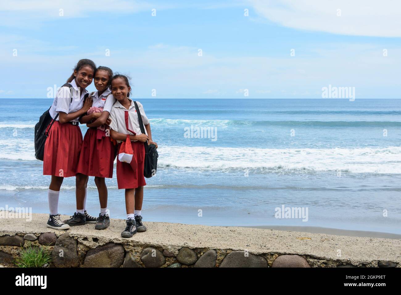 Tres alegres niñas escolares con uniformes escolares rojos y blancos que regresan a casa de la escuela. Pueblo de Sikka, Isla Flores, Nusa Tenggara Oriental, Indonesia. Foto de stock