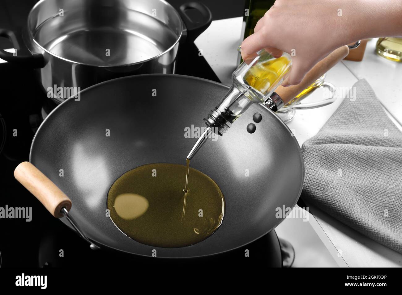 Mujer vertiendo aceite de la botella en wok en la cocina Fotografía de  stock - Alamy