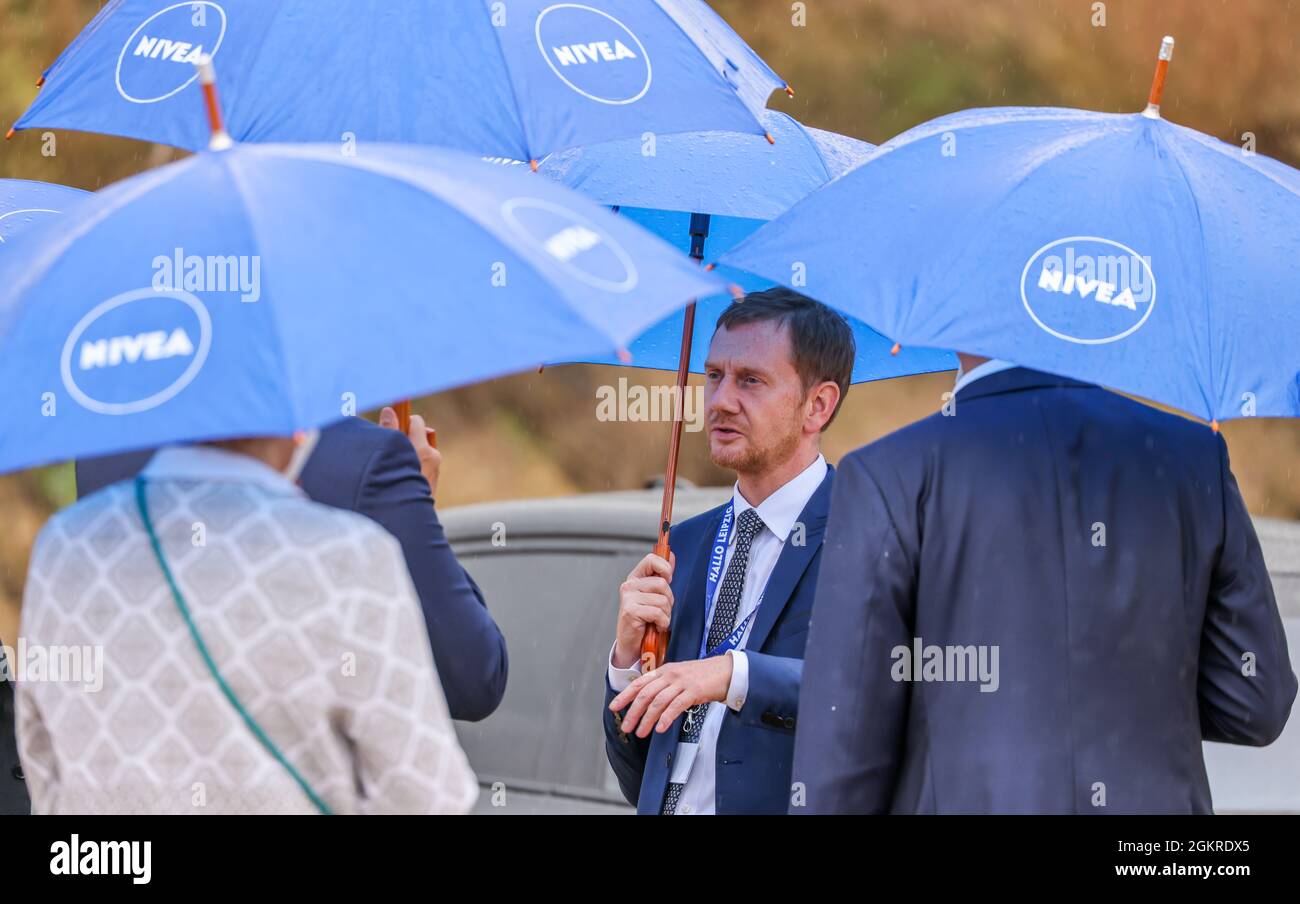 15 de septiembre de 2021, Sajonia, Leipzig: Michael Kretschmer (CDU),  Ministro Presidente de Sajonia, habla con representantes de la empresa bajo  paraguas con el logotipo de Nivea antes de colocar la piedra
