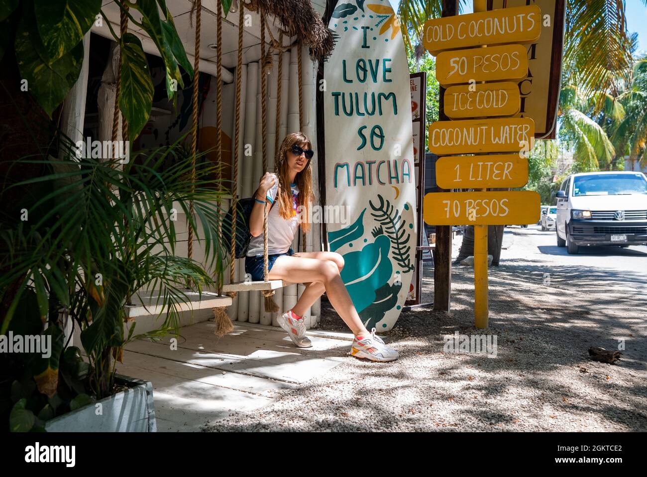 Mujer sentada en el asiento oscilante de la tienda de coco con menú de bebidas al lado de la carretera Foto de stock
