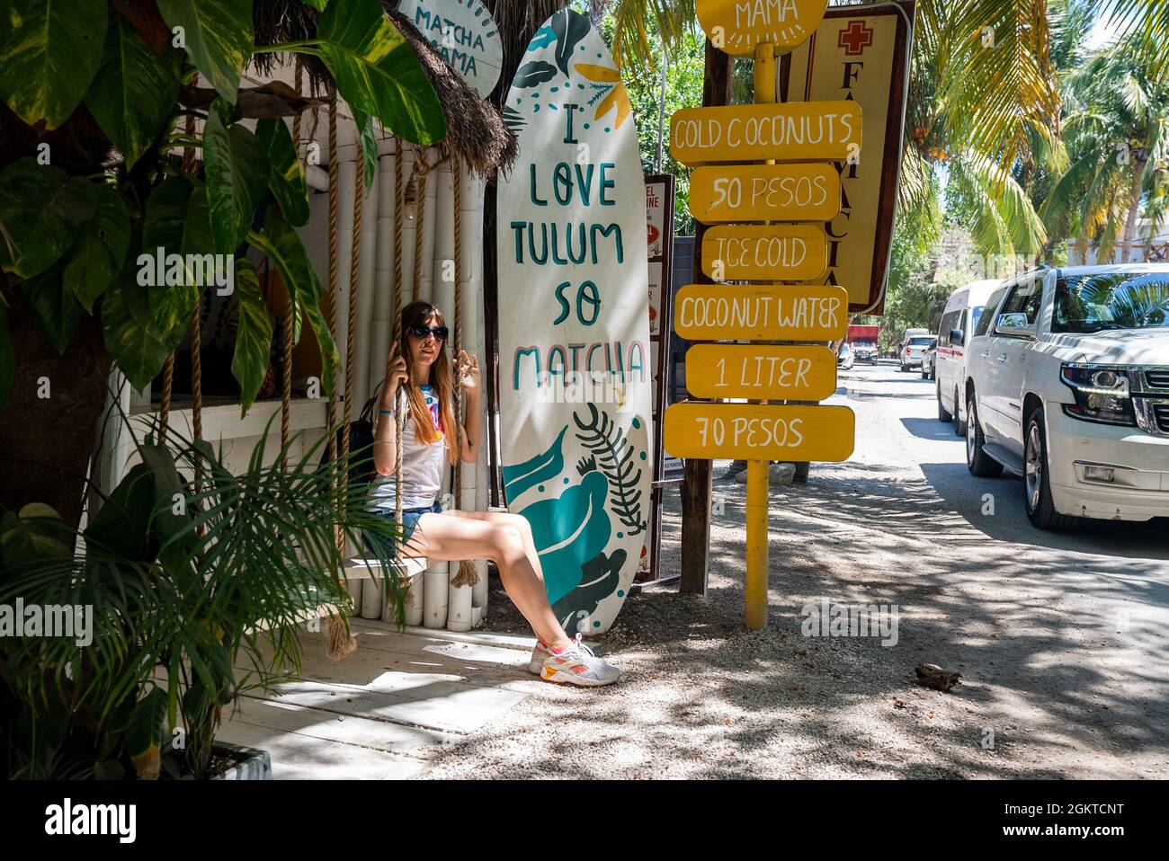 Mujer sentada en el asiento oscilante de la tienda de coco con menú de bebidas al lado de la carretera Foto de stock