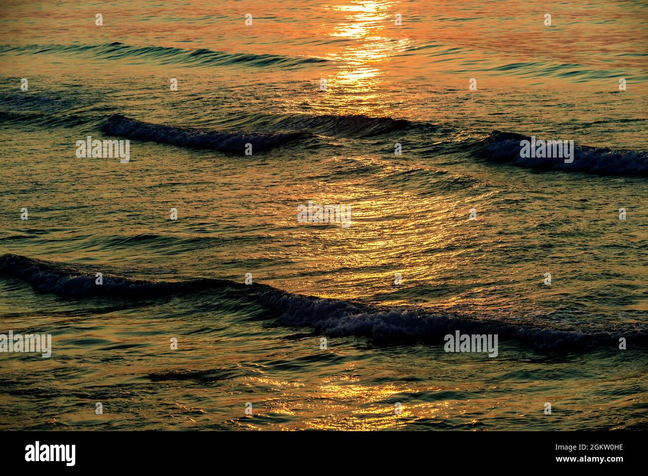El sol naciente arrojó su luz reflejada a través de las olas, y ondulaciones de la marea entrante del océano. Al igual que crea diseños abstractos. Foto de stock