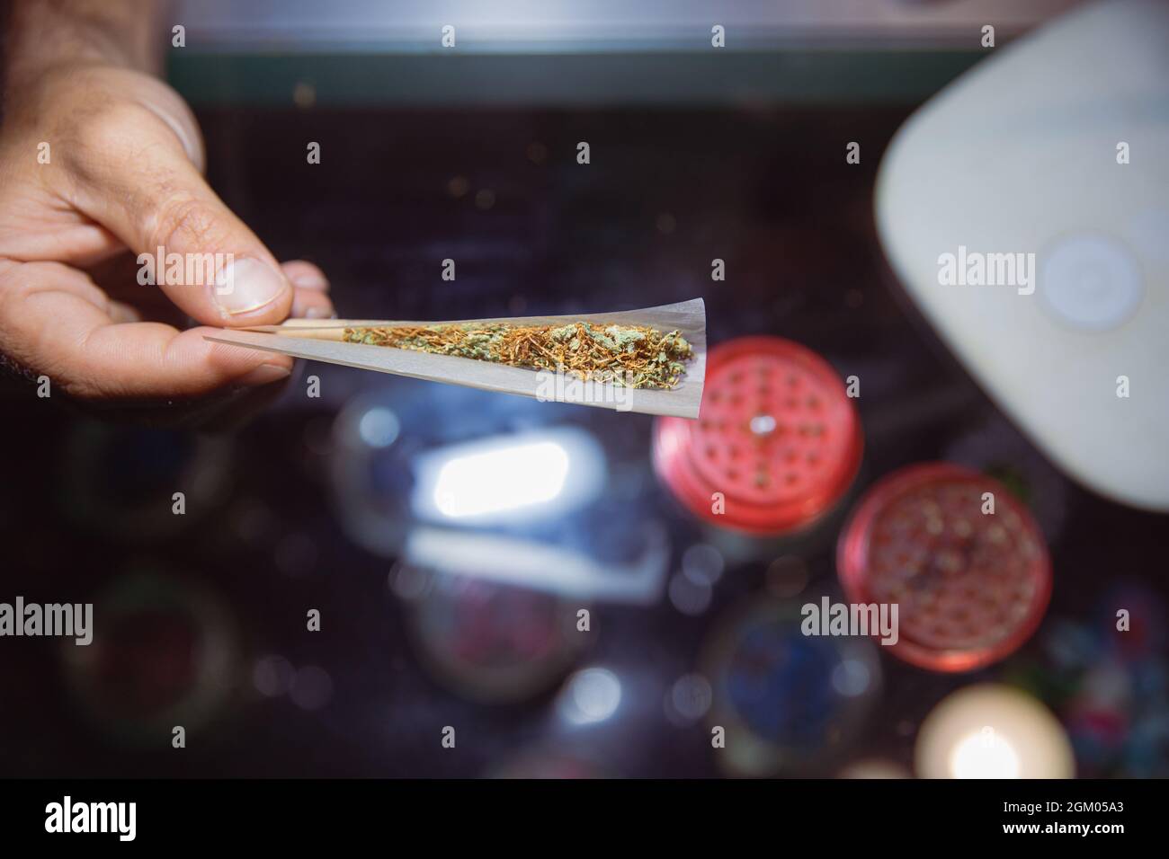 El primer plano de una articulación de marihuana se abrió mientras rodaba. Molinillo abierto en el fondo. Proceso de fabricación de una articulación de marihuana Foto de stock