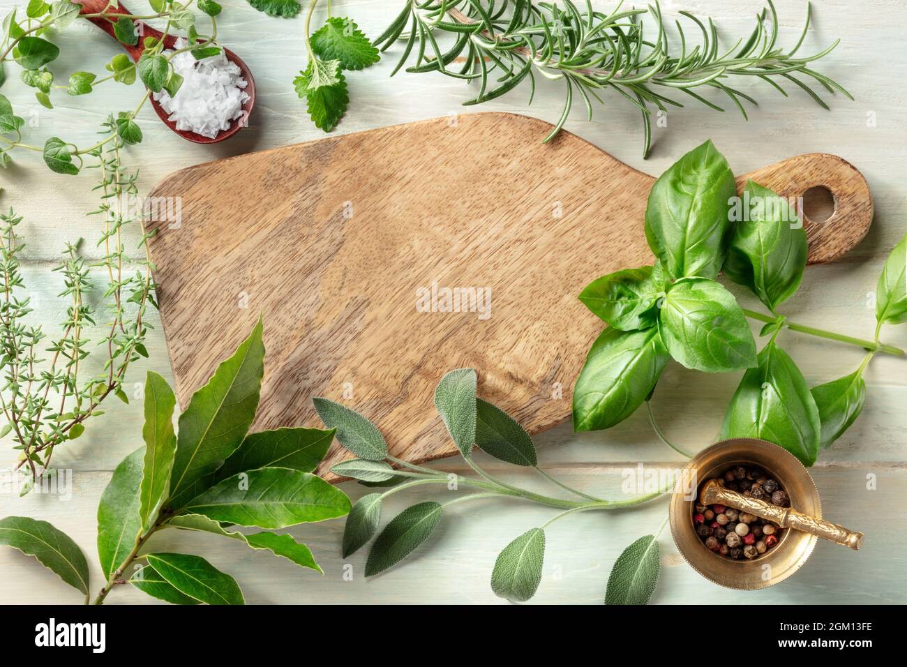 Cocinar con hierbas. Una tabla de cortar de madera con sal, pimienta y hierbas aromáticas. Albahaca, hoja de laurel, romero, tomillo, salvia, orégano, y bálsamo de limón Foto de stock