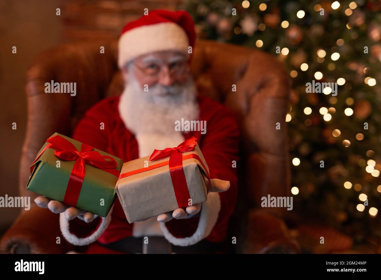 Papá Noel sentado en el sillón y regalando regalos de Navidad atados con  cintas rojas a la cámara Fotografía de stock - Alamy