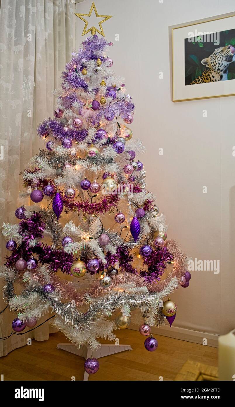 Árbol de Navidad artificial blanco decorado con adornos lila y de color púrpura Foto de stock