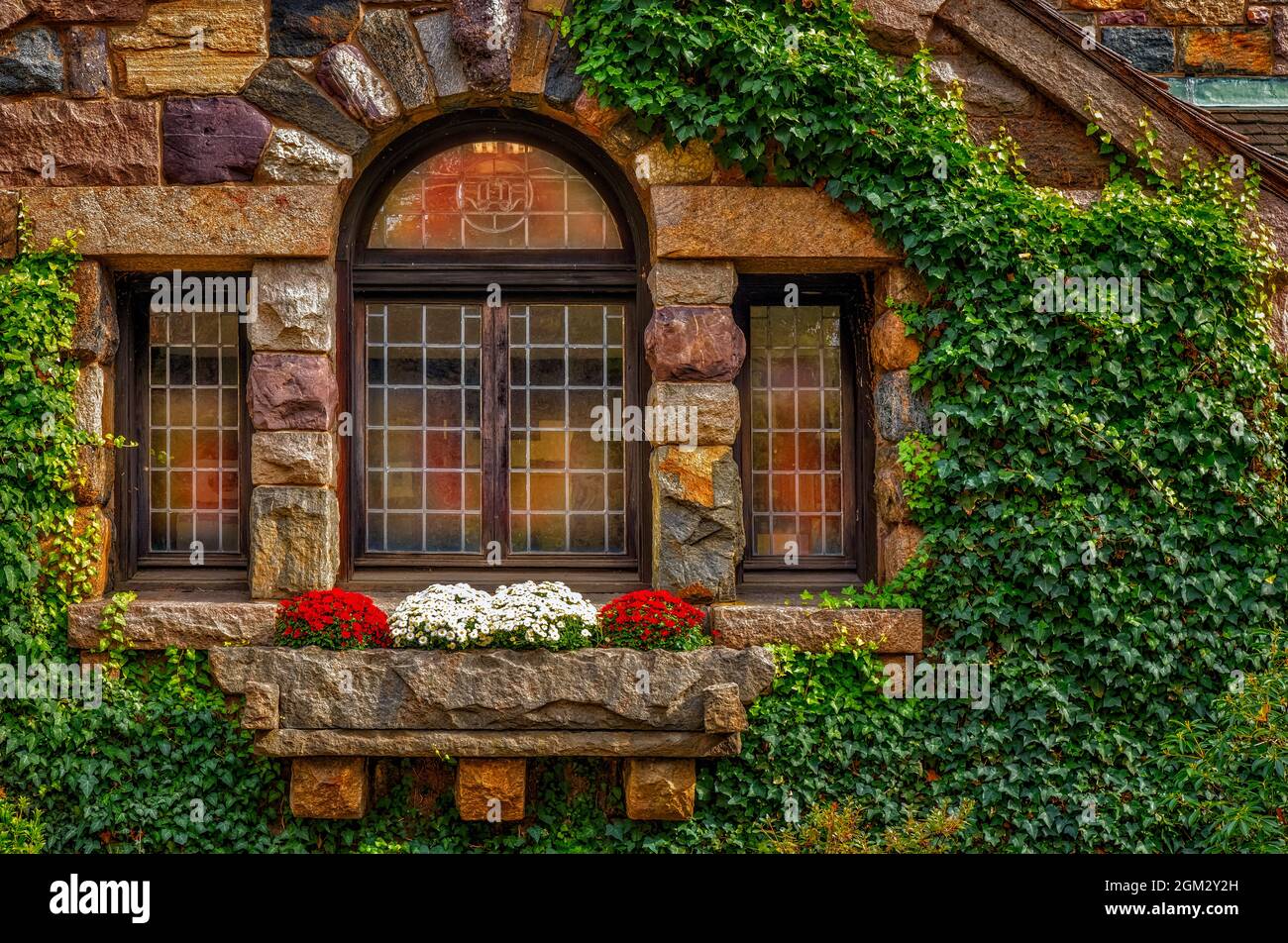 Otoño reflectante - Antigua estructura de piedra con ventanas que reflejan los colores del otoño. También se ven flores de cristhantemos en la caja de flores. Este yo Foto de stock