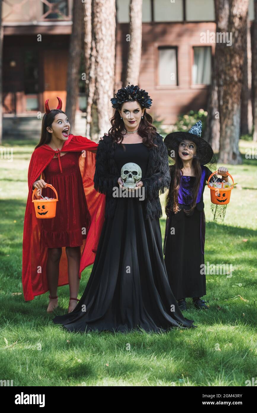 mujer en vampiro traje de halloween sosteniendo el cráneo cerca de hijas  espeluznantes con cubos de dulces Fotografía de stock - Alamy