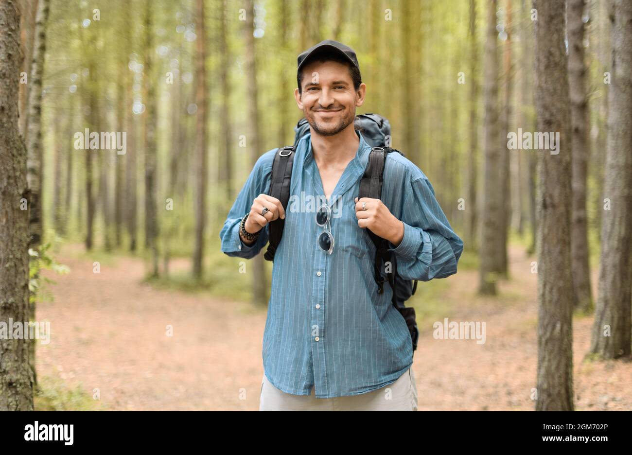 Hombre sonriente, de 40 años, con su mochila turística está parado en un bosque. Foto de stock