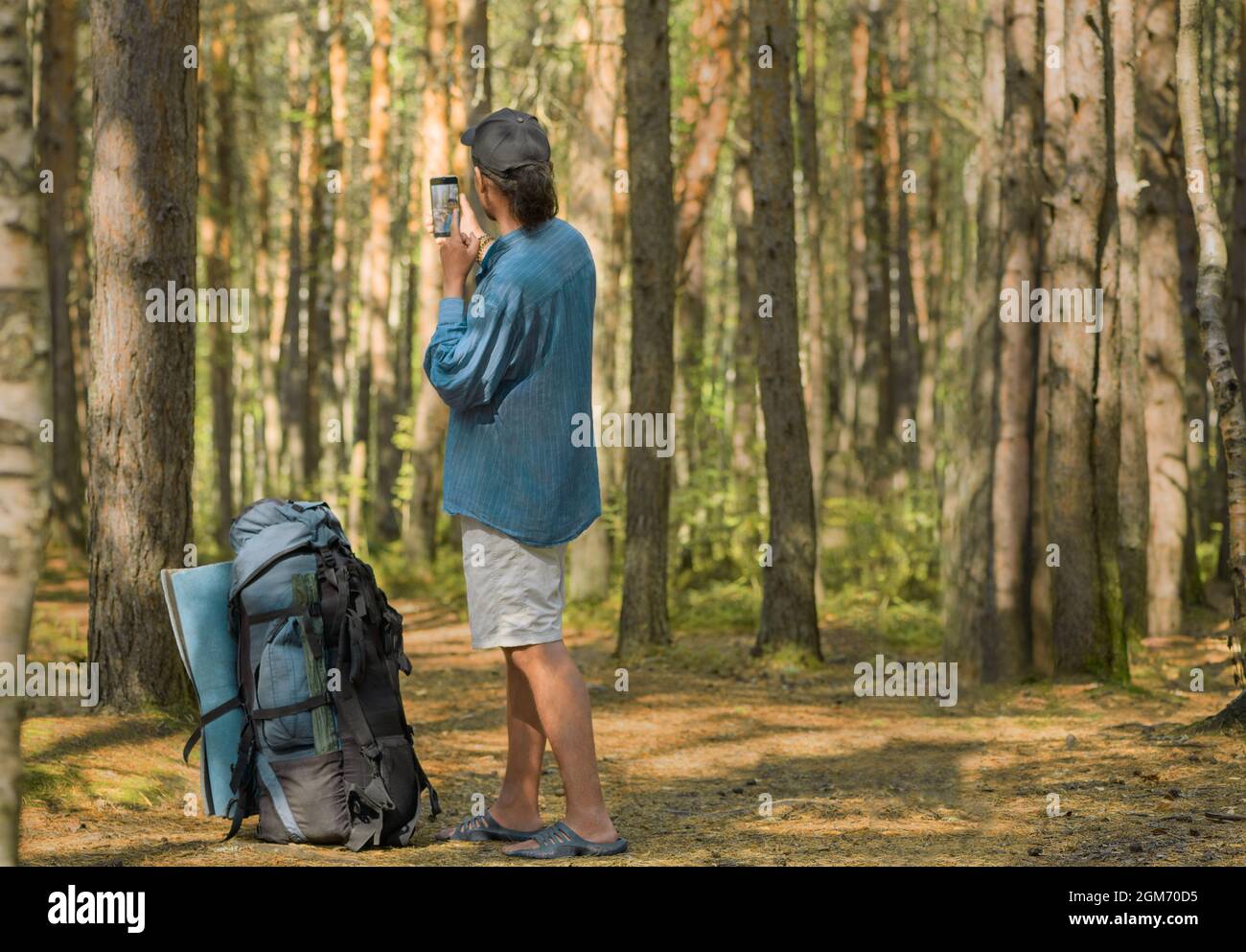 El hombre caucásico con su gran mochila turística está tomando una selfie en un bosque. Foto de stock