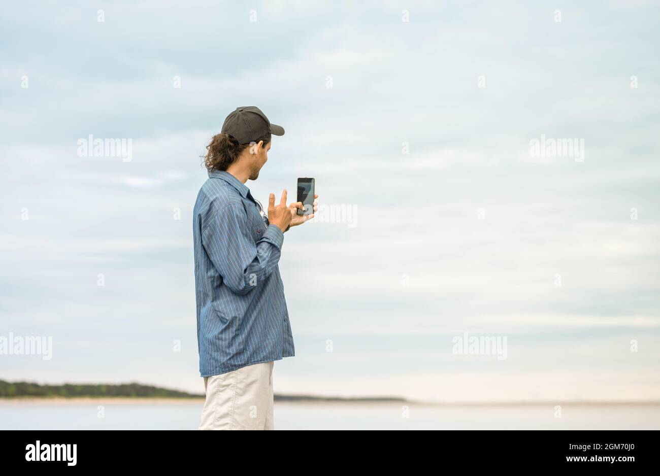 El hombre caucásico con está sosteniendo un smartphone en su mano y tomando una selfie en una playa. Foto de stock
