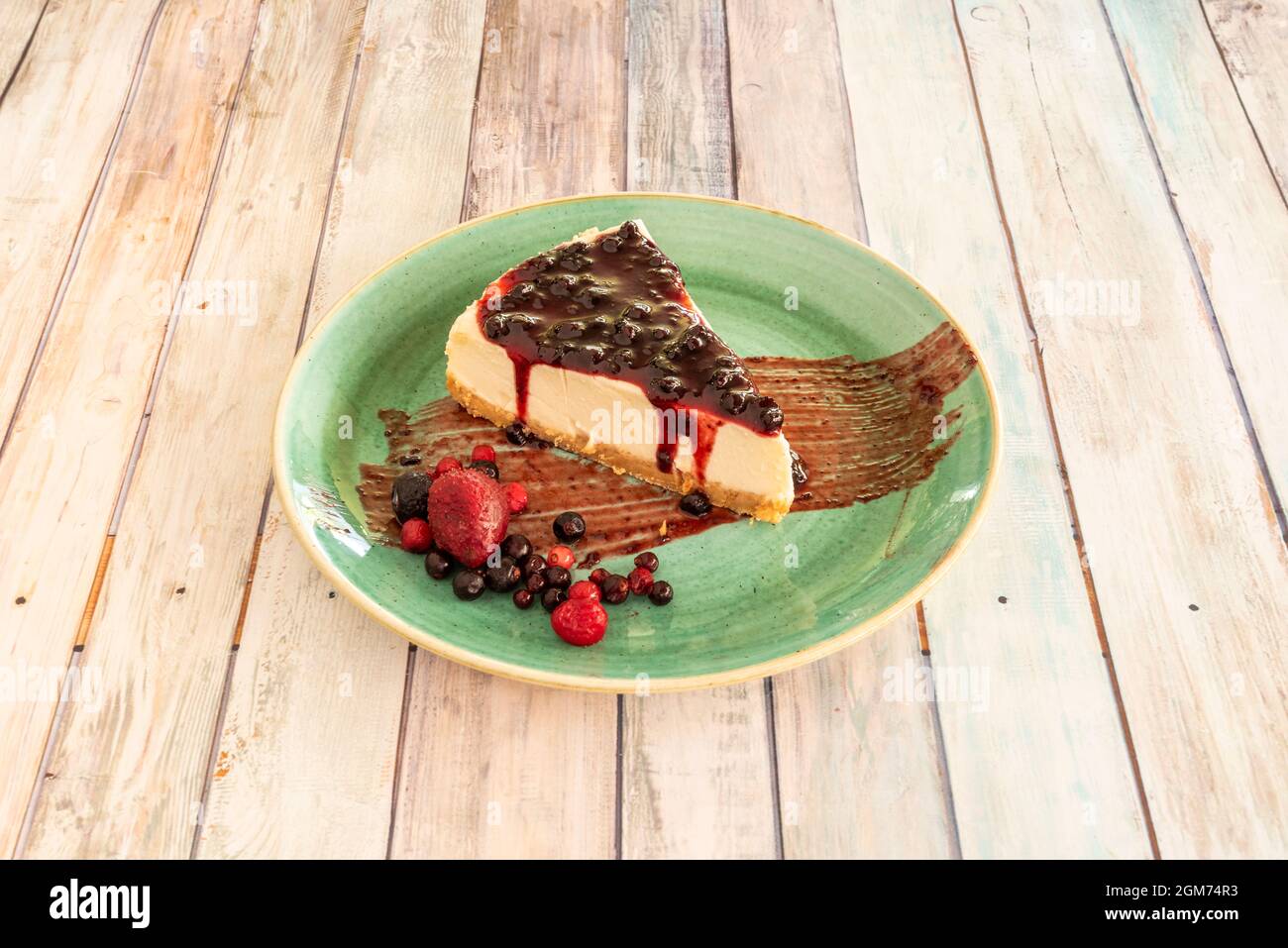 Increíble presentación de tarta de queso con mermelada de bayas rojas y bayas con fresas en el plato verde Foto de stock