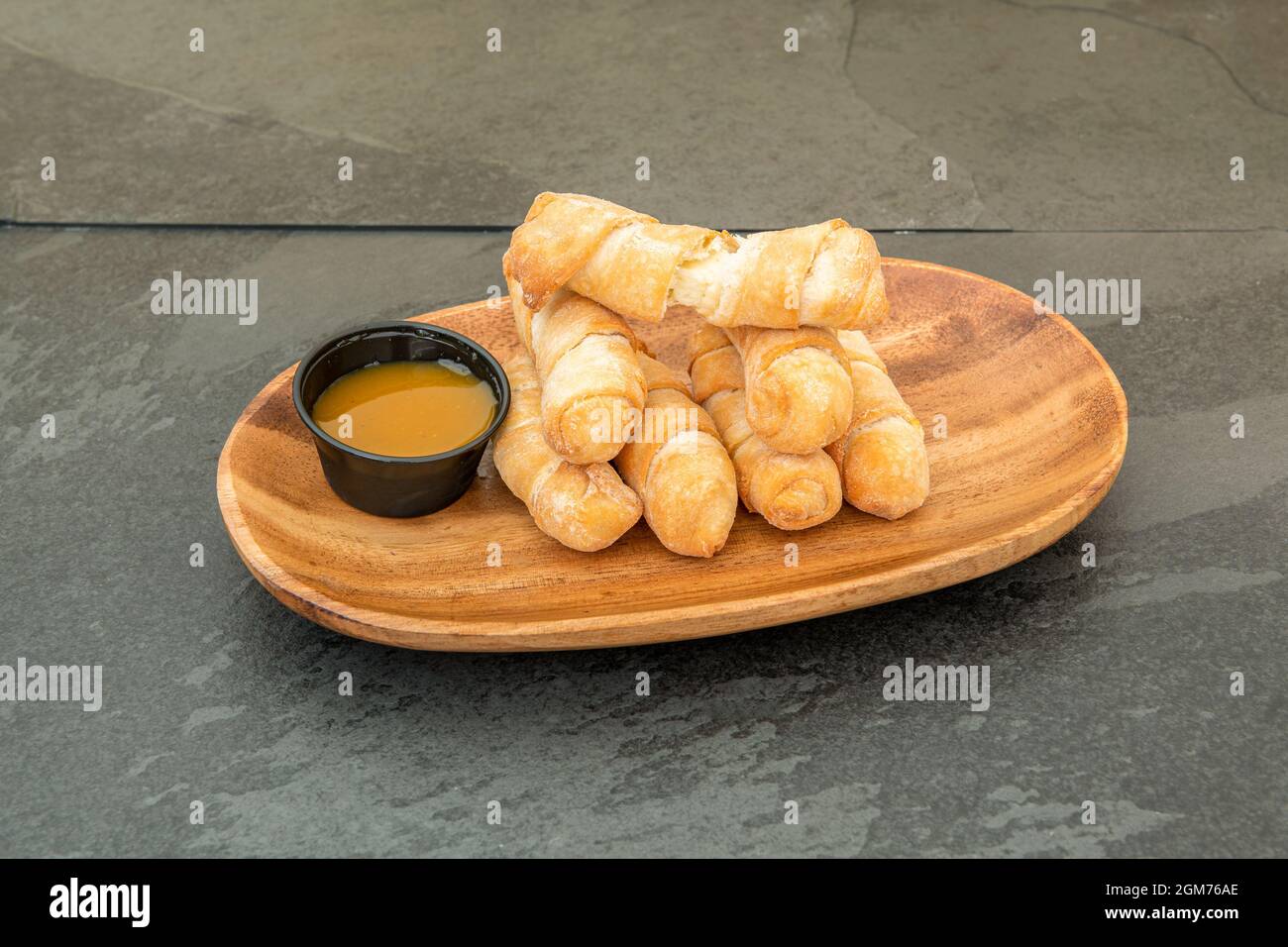 Bandeja de madera con tequeños para el desayuno con uno de ellos en la  parte superior dividido en la mitad en una mesa de pizarra negra Fotografía  de stock - Alamy