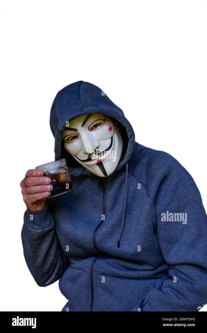 teorista de conspiración masculina anti vacuna usando hoodie y v para los tostadas con máscara de vendetta con un vaso de alcohol Foto de stock