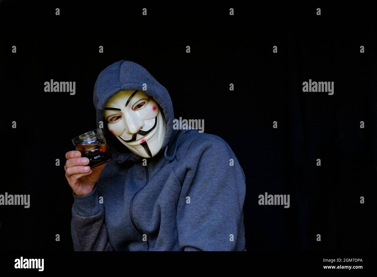 teorista de conspiración masculina anti vacuna usando hoodie y v para los tostadas con máscara de vendetta con un vaso de alcohol Foto de stock