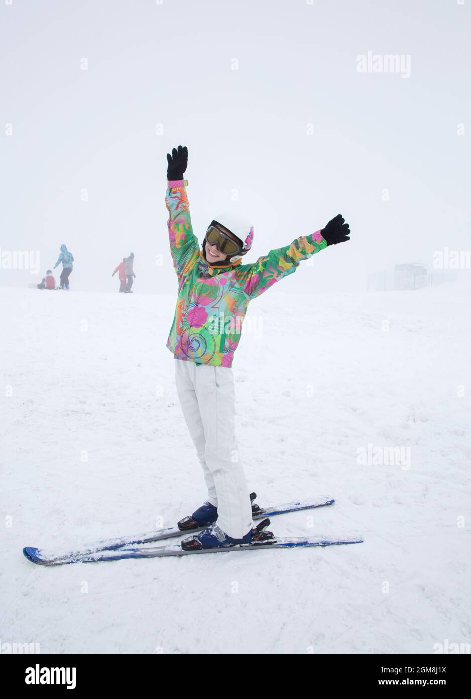 hermosa niña de 16 años de humor alegre está esquiando en la ladera de una montaña con las manos levantadas. Interesantes vacaciones de invierno activas Foto de stock