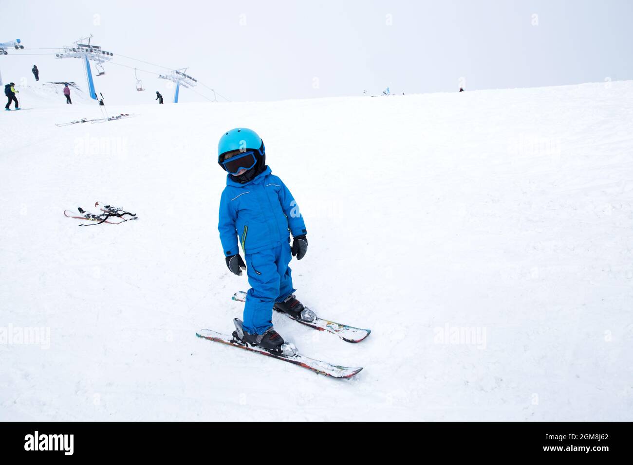 el niño en casco, gafas, esquís y monos azules se encuentra en la ladera  nevada. Clase de esquí para niños en la escuela de esquí. Entretenimiento  activo en invierno f Fotografía de