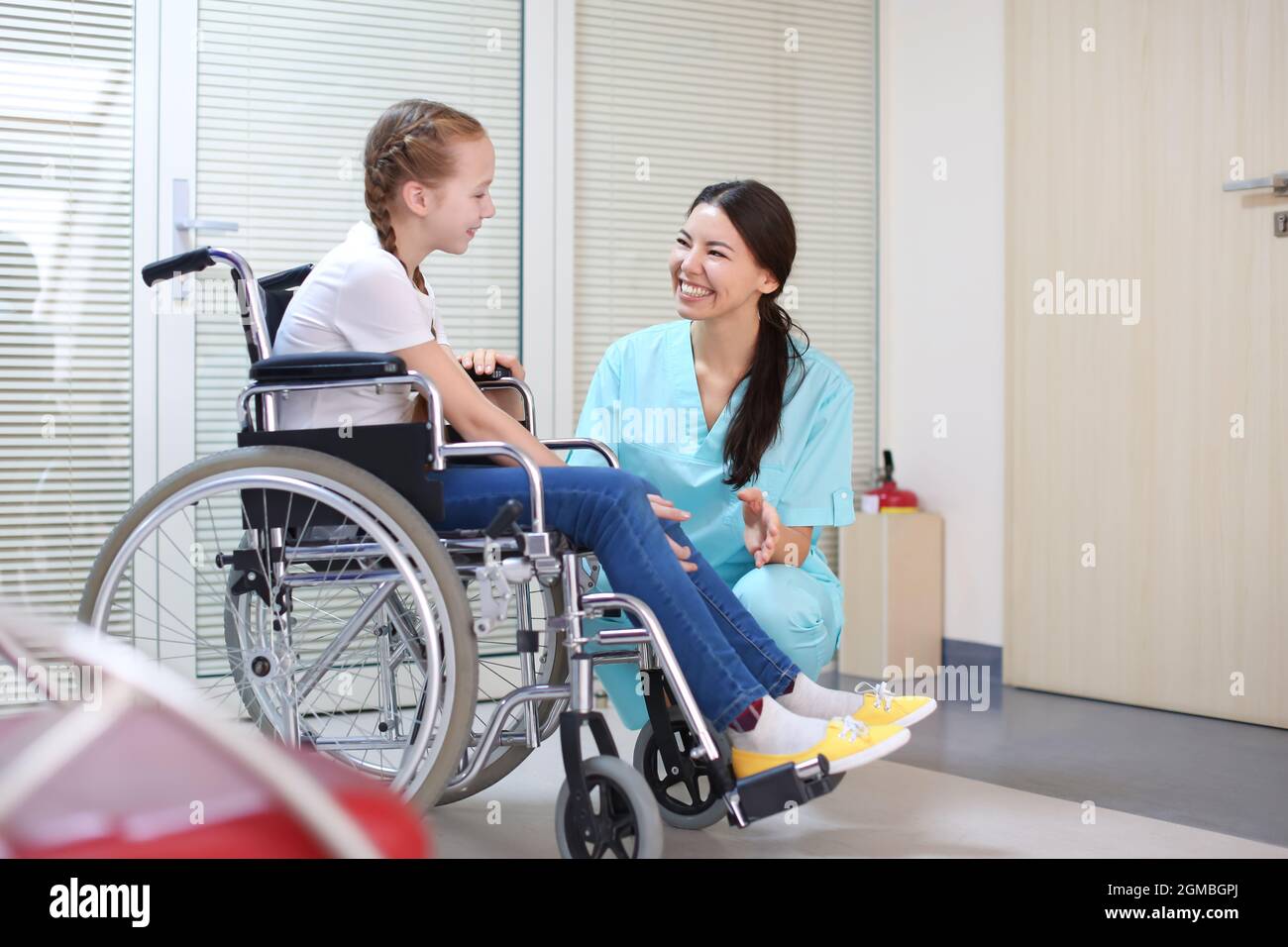 Joven doctora teniendo cuidado de niña en silla de ruedas en el interior Foto de stock