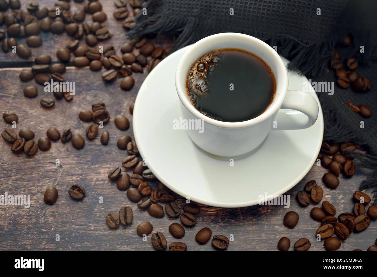 Café negro intenso en una taza blanca sobre una mesa de madera rústica oscura con algunos frijoles, espacio de copia, enfoque seleccionado, profundidad de campo estrecha Foto de stock