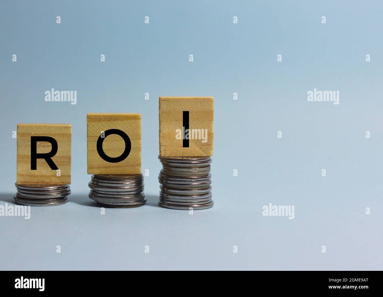 ROI o retorno de la inversión acrónimo escrito en cubos de madera encima de las monedas apiladas hacia arriba. Espacio de copia. Foto de stock