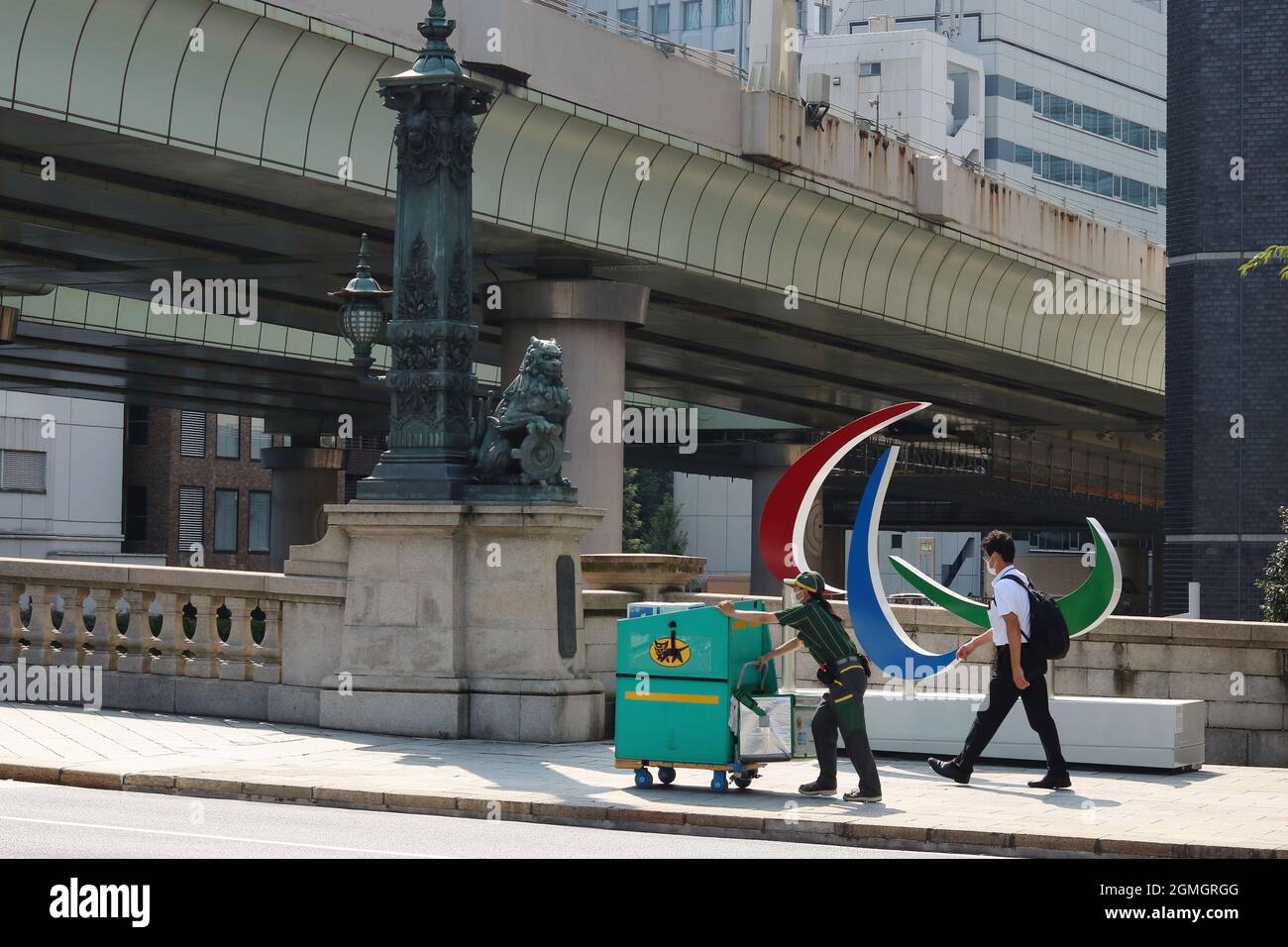 La gente, incluido un trabajador de reparto de Yamato, pasa por un monumento con el símbolo paralímpico junto a una estatua de un león en el puente de Nihonbashi durante los Juegos Paralímpicos de Tokio. Foto de stock