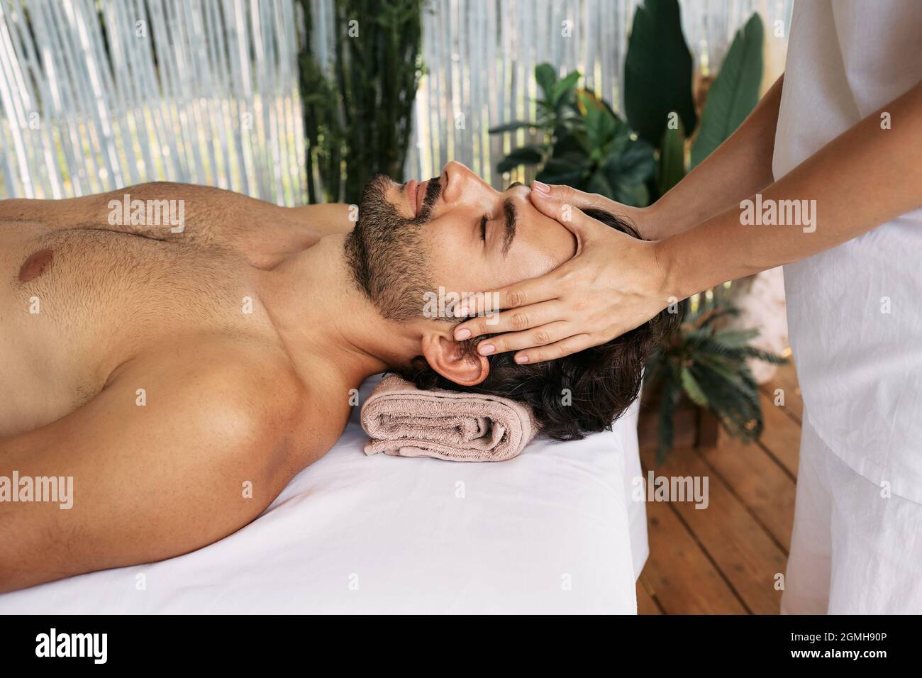 El hombre relajado recibe un masaje de cabeza en el spa. Masaje de cabeza antiestrés, vista lateral Foto de stock