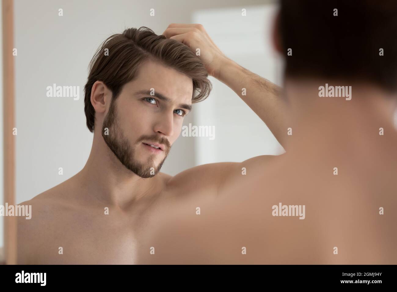El hombre mira en el espejo de tacto del cabello se siente preocupado debido a la caída Foto de stock