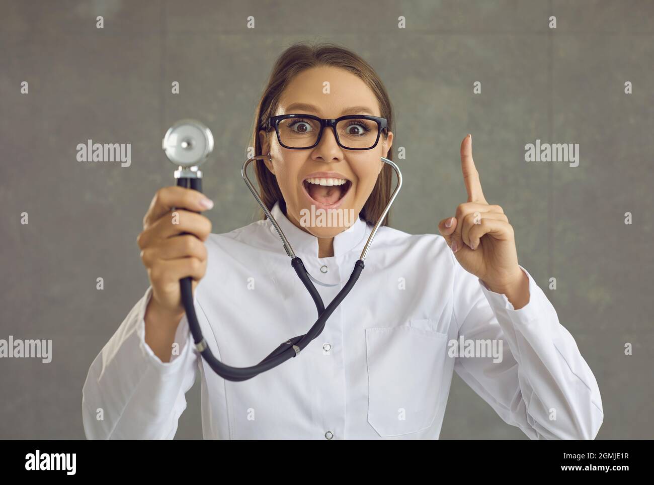 Retrato de un doctor feliz con estetoscopio apuntando un dedo hacia arriba golpeado por una gran idea Foto de stock
