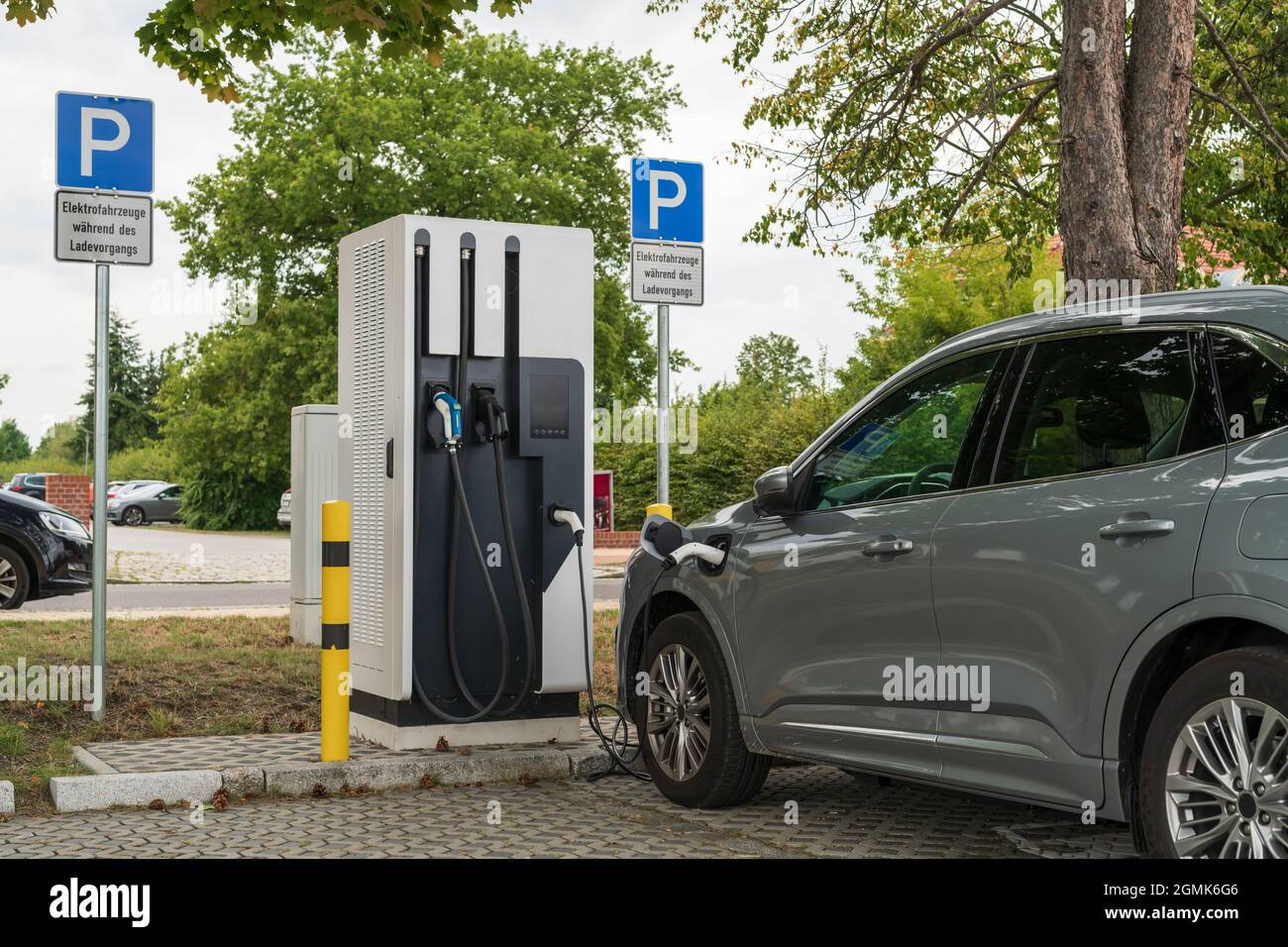Un coche en una estación de carga y en la señal de estacionamiento es la señal adicional con el texto alemán 'Vehículos eléctricos durante la carga' Foto de stock