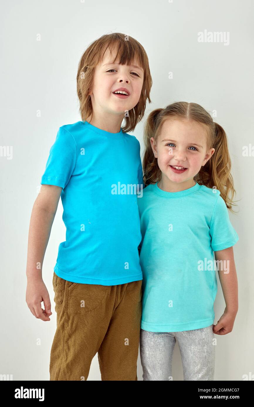 Alegre niña y niño preescolar en camiseta azul brillante abrazando y  mirando la cámara mientras se encuentra de pie contra la pared blanca  Fotografía de stock - Alamy