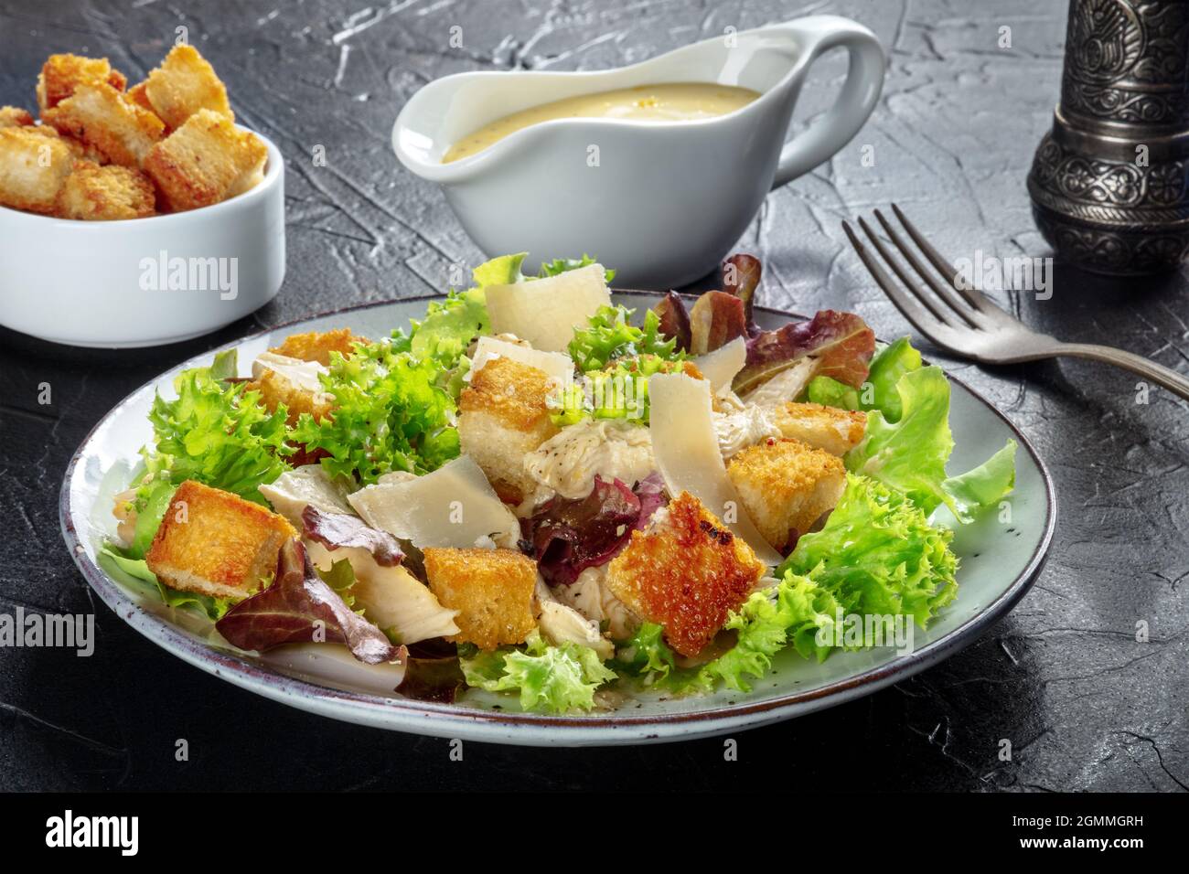 Ensalada César de pollo con aderezo clásico, croutones y pimienta, sobre fondo negro Foto de stock