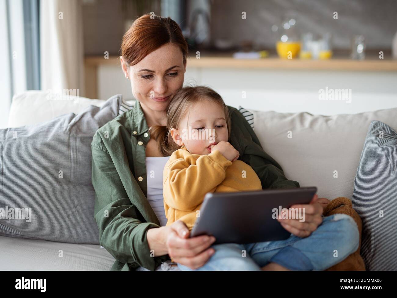 Feliz madre con hija pequeña viendo a los niños programa en la tableta interior en el hogar, concepto de crianza única. Foto de stock
