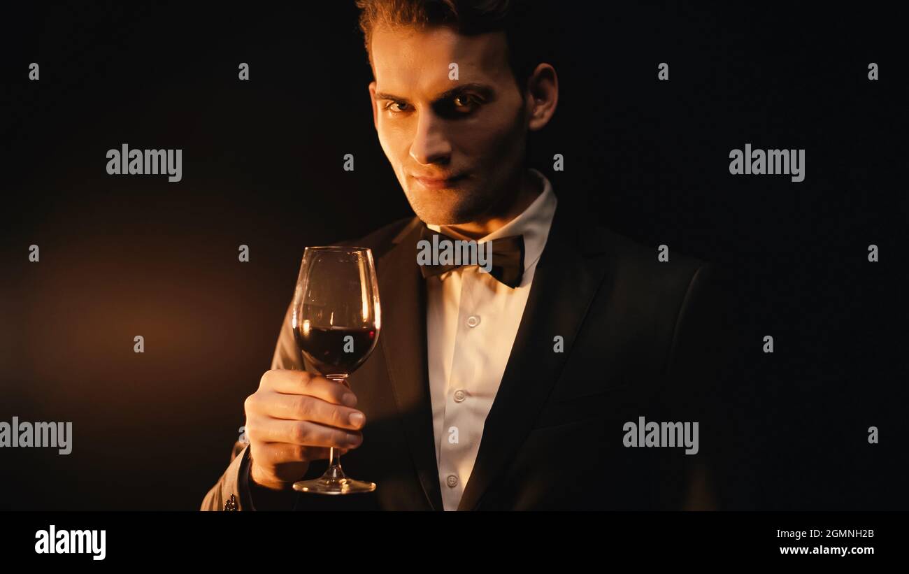 hombre-joven-elegante-en-traje-con-lazo-que-sostiene-una-copa-de-vino-en-negro-2gmnh2b.jpg