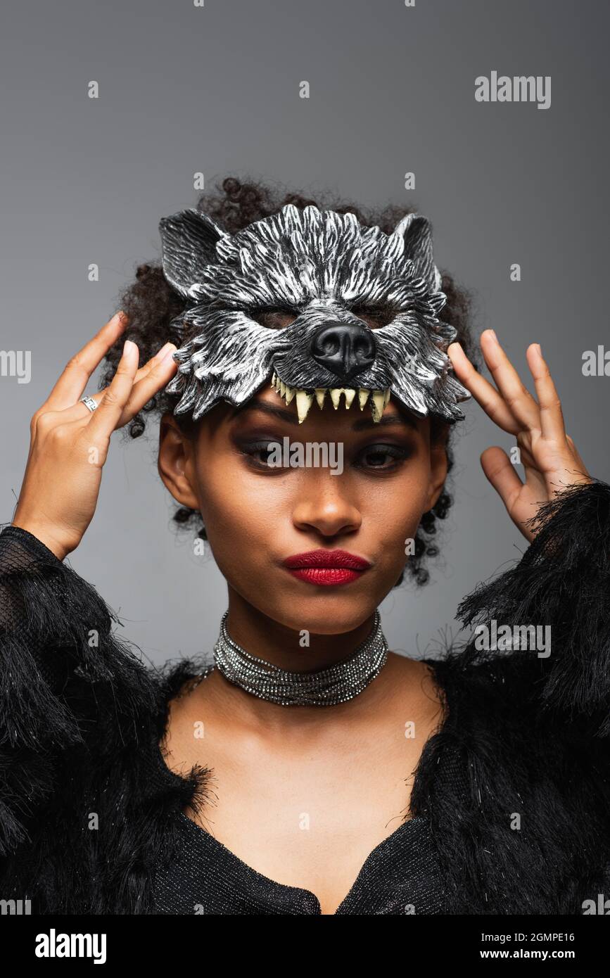 disgustada mujer afroamericana ajustando máscara de halloween de hombre lobo  aislado en gris Fotografía de stock - Alamy