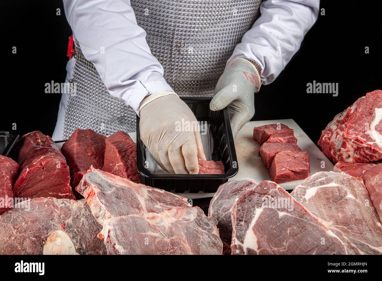 Carnicero cortando carne. Chef en guantes de látex blanco sosteniendo  trozos de carne cruda sobre una tabla de corte de poliuretano blanco, sobre  un fondo oscuro Fotografía de stock - Alamy
