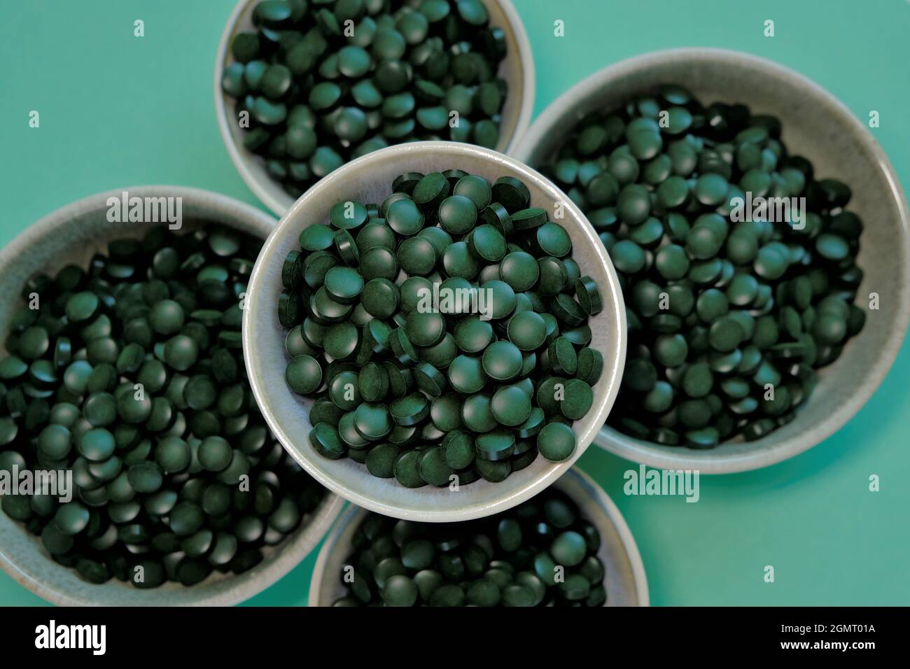 Tabletas de algas Spirulina. Pastillas de Spirulina en tazas sobre fondo verde. Omega tres. Origen vegetal de aminoácidos y omega 3. Foto de stock