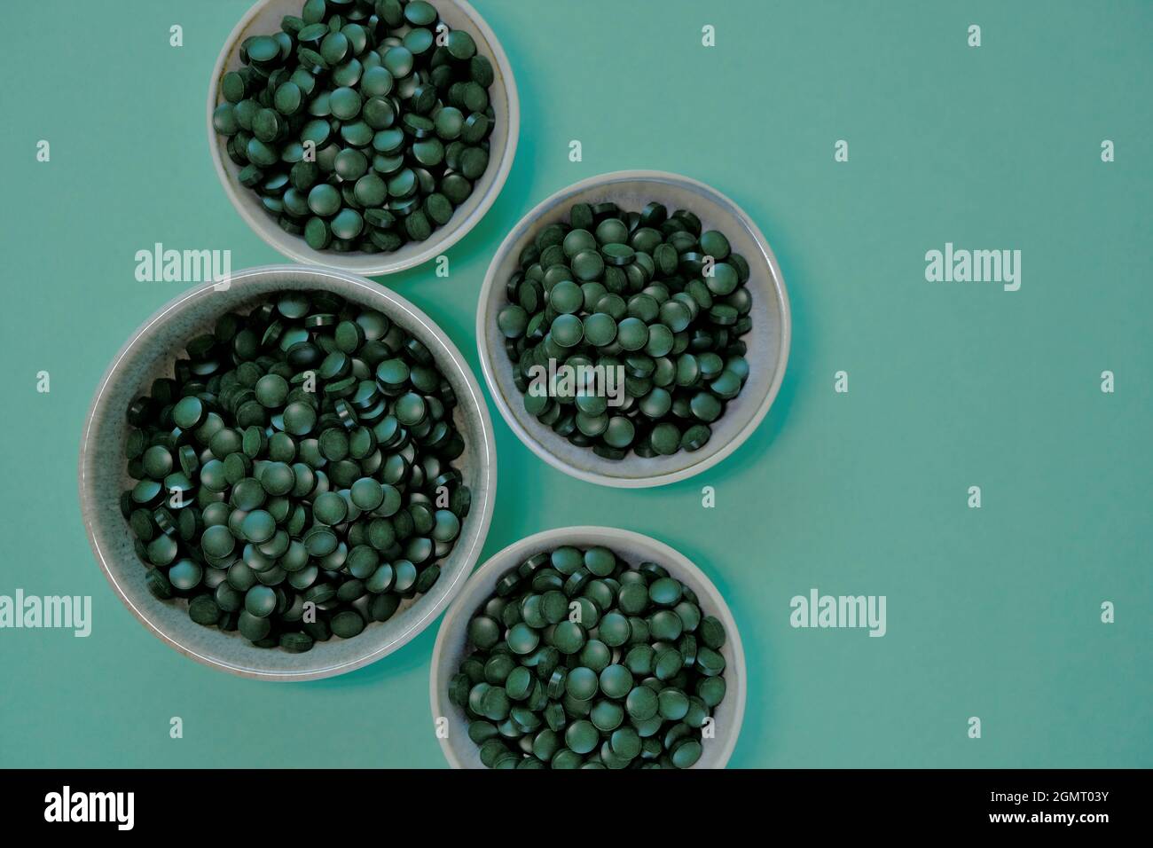 Tabletas de algas Spirulina. Pastillas de Spirulina en tazas sobre fondo verde. Omega tres. Origen vegetal de aminoácidos y omega 3. La comida era estupenda Foto de stock