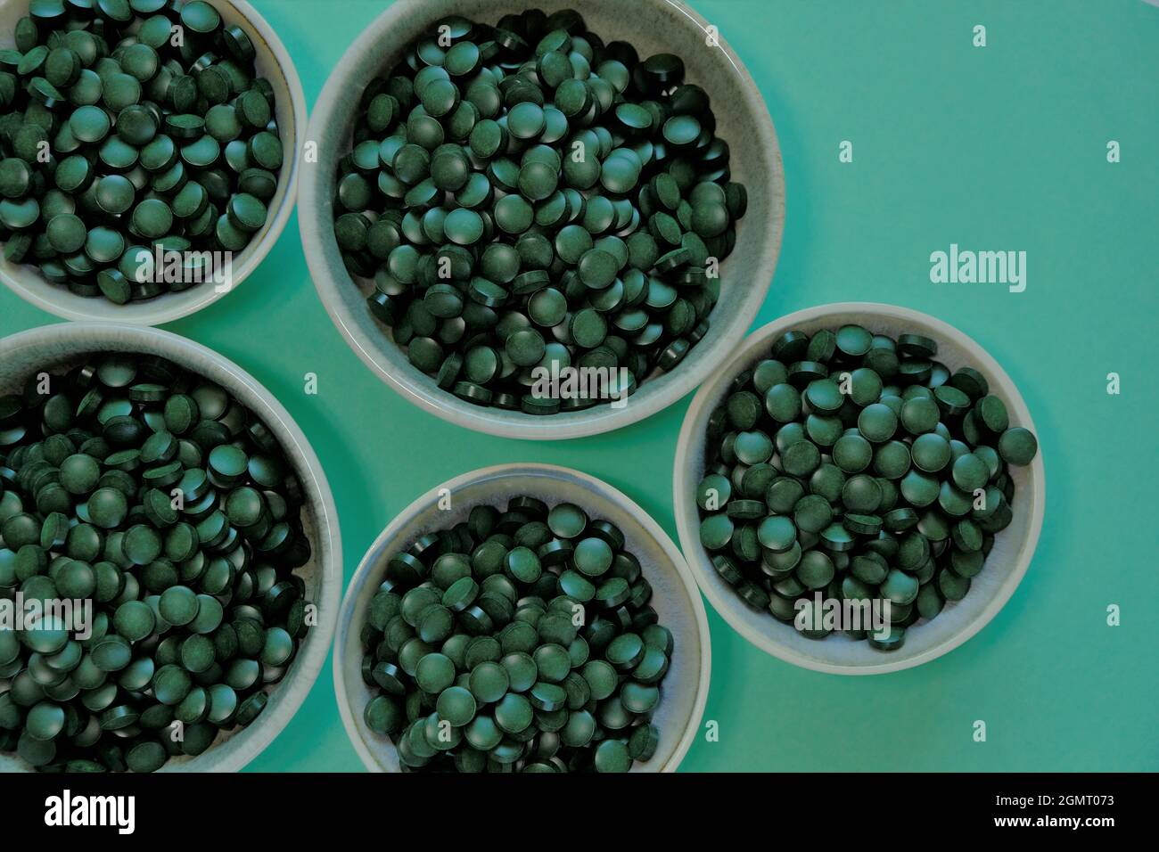 Tabletas de algas Spirulina. Pastillas de Spirulina en tazas sobre fondo verde. Omega tres vegetariano.Fuente de la planta de aminoácidos y omega 3.Omega tres Foto de stock
