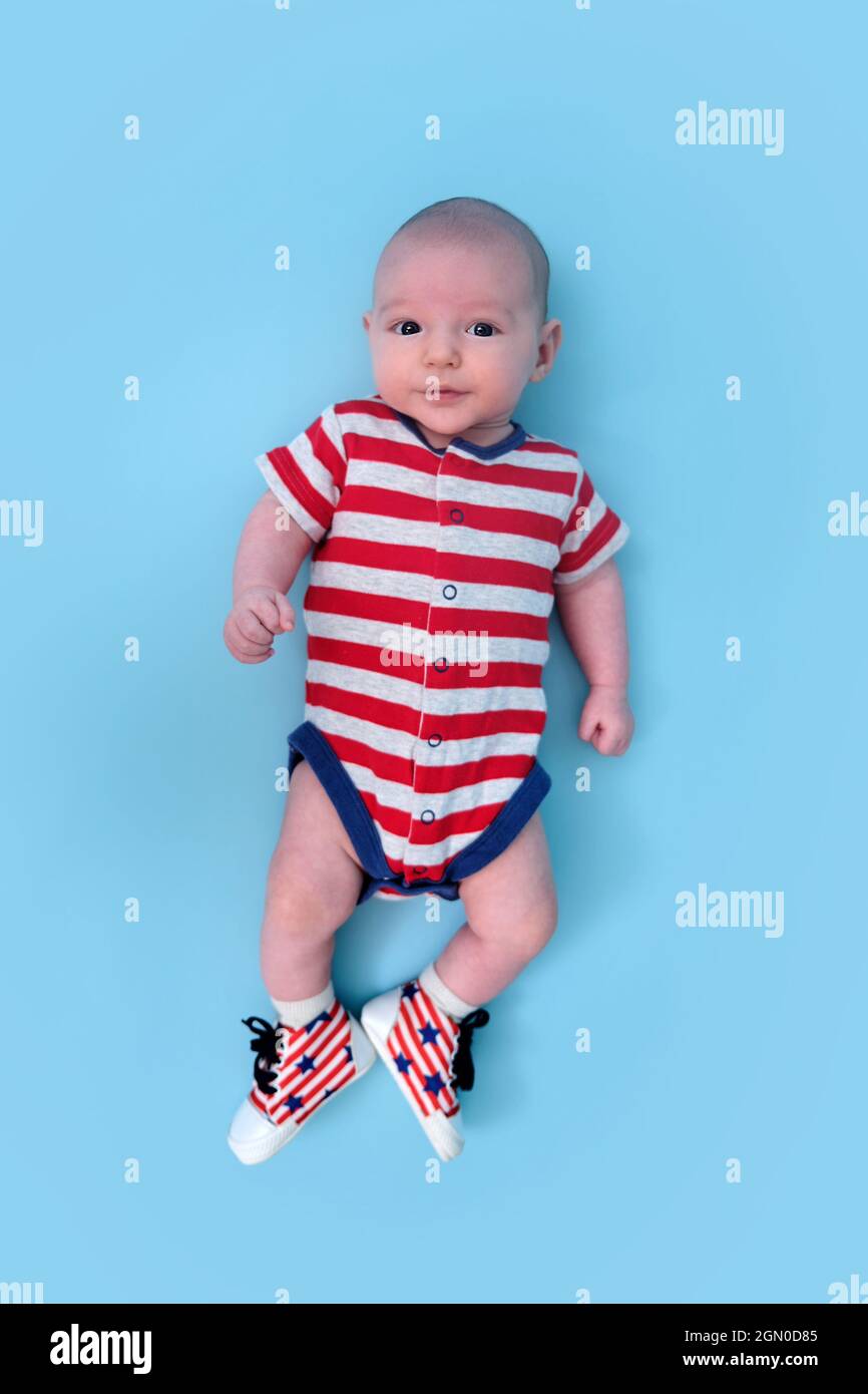 Un bebé recién nacido vestido con los colores la bandera americana de los Estados Unidos, fondo azul del estudio. Un niño en la ropa de los EE.UU. Rojo y blanco Fotografía