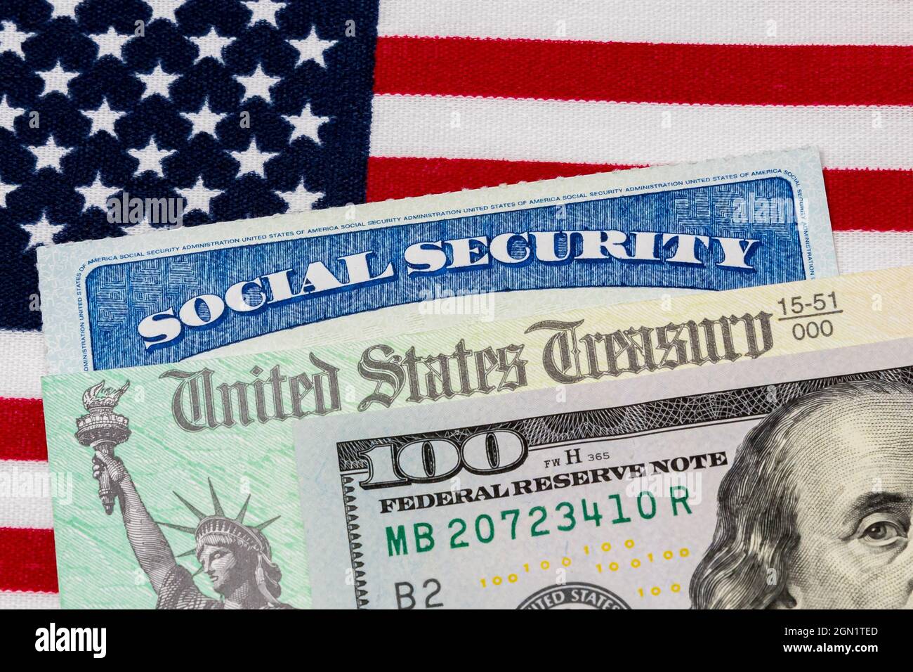 Tarjeta de seguridad social, cheque de tesorería, billete de 100 dólares y bandera estadounidense. Concepto de pago de prestaciones de seguridad social, jubilación y gobierno federal Foto de stock