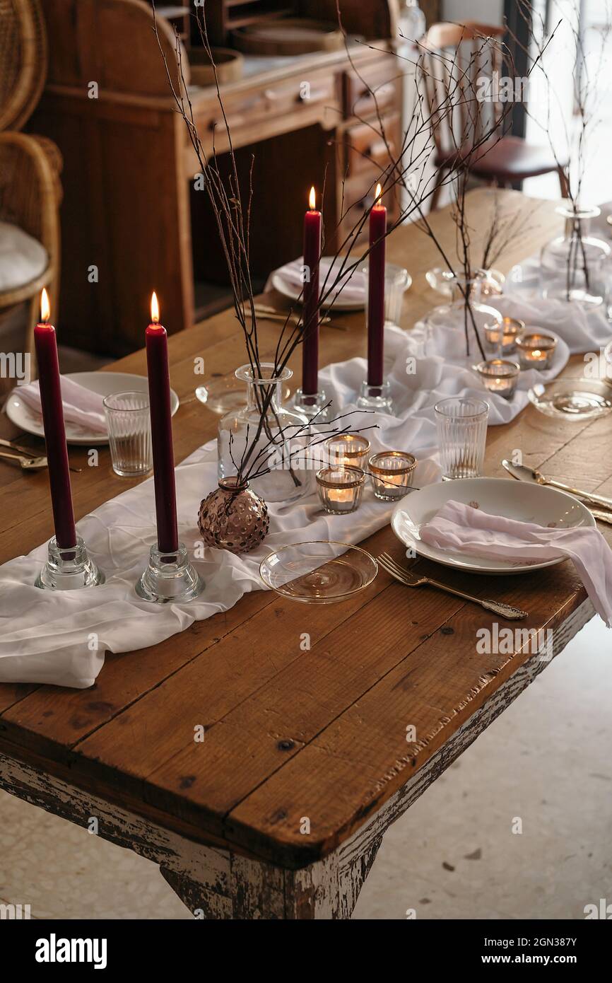 Mantel blanco y platos colocados sobre mesa festiva decorada con velas  encendidas y ramas secas de árbol Fotografía de stock - Alamy